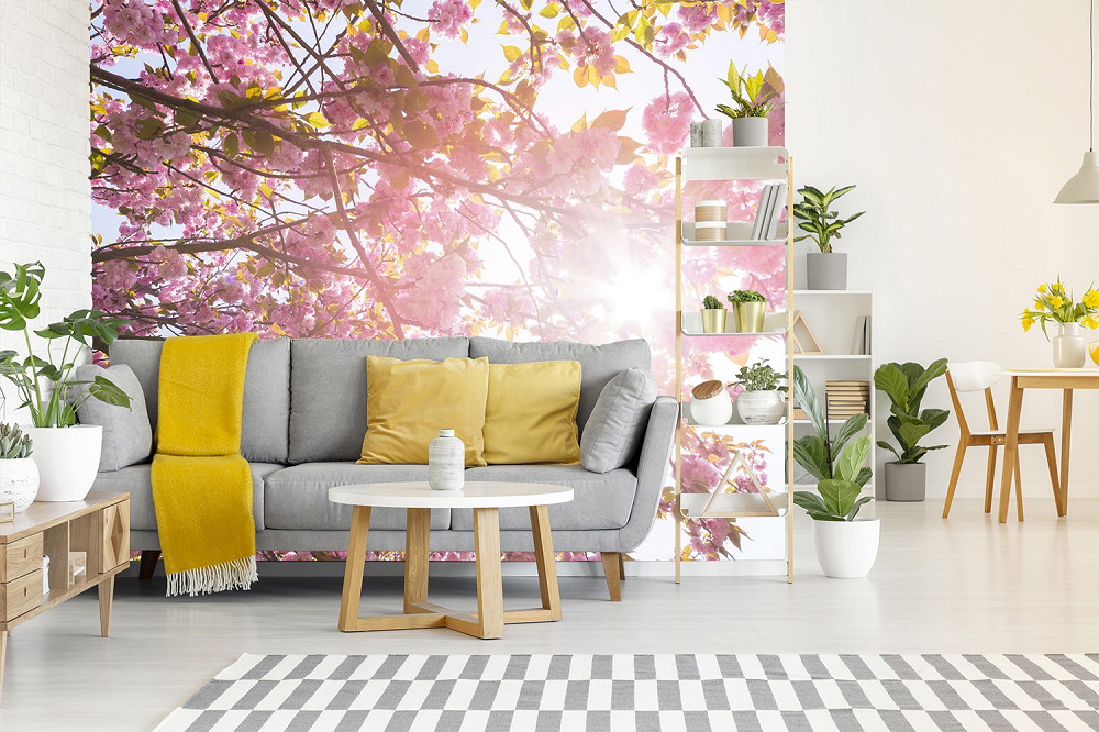 Fototapete - Modernes Wohnzimmer mit Kirschblüten-Wandbild, grauem Sofa und gelben Kissen