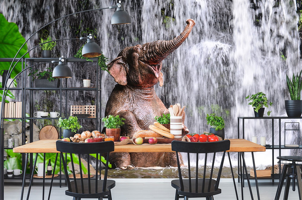 Wall mural - An elephant enjoying a refreshing waterfall in a modern decorated kitchen with plants and fruit basket