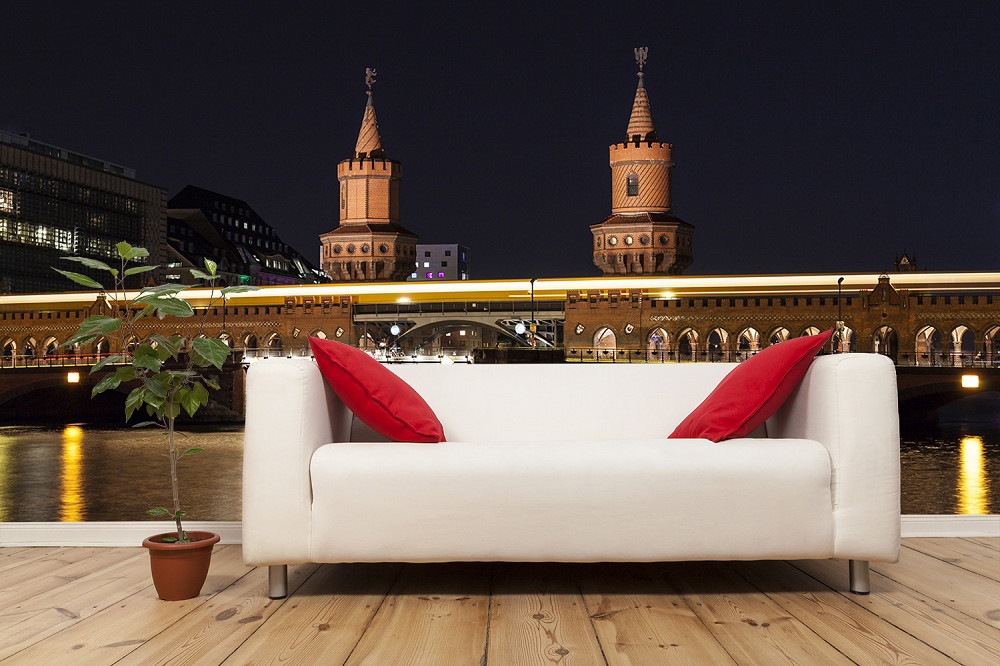 Fotobehang - Woonkamer met witte bank en rode kussens tegen de achtergrond van de nachtelijke skyline van Berlijn