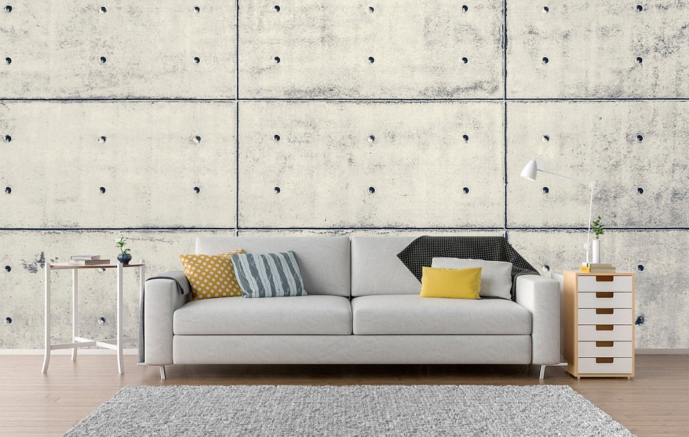 Muurschildering - Woonkamer met grijze betonnen muur, een witte bank, kleurrijke kussens en minimalistische inrichting