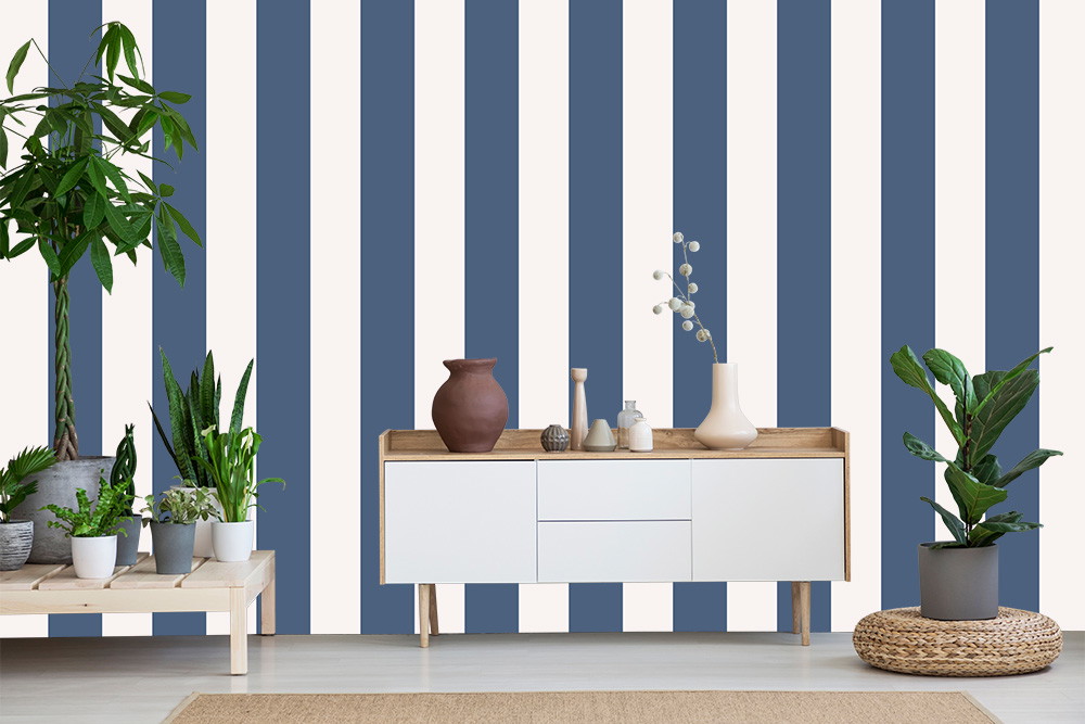 Fotomurale - Soggiorno con carta da parati a righe bianche e blu, credenza bianca e varie piante da appartamento