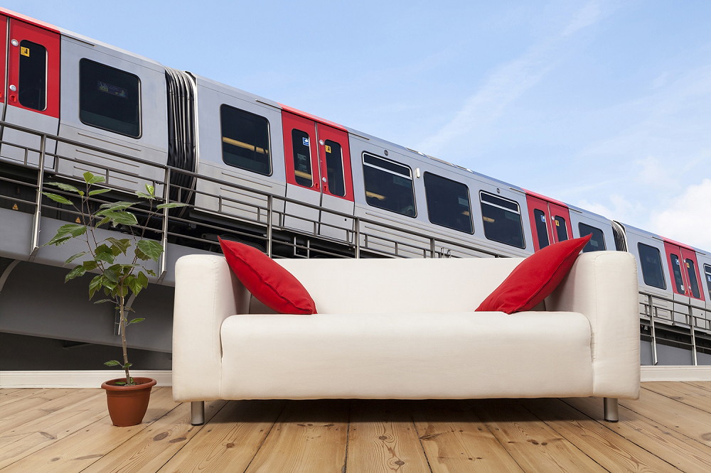 Wall mural - Light rail in modern design with red accent travelling behind a white sofa with red cushions and potted plant