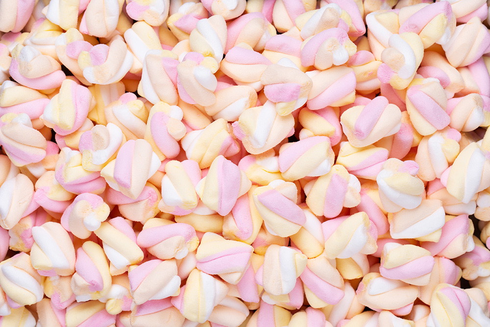 Muurschildering - Een verscheidenheid aan kleurrijke mini-marshmallows in pastelroze, geel en wit die als zoete achtergrond dienen.