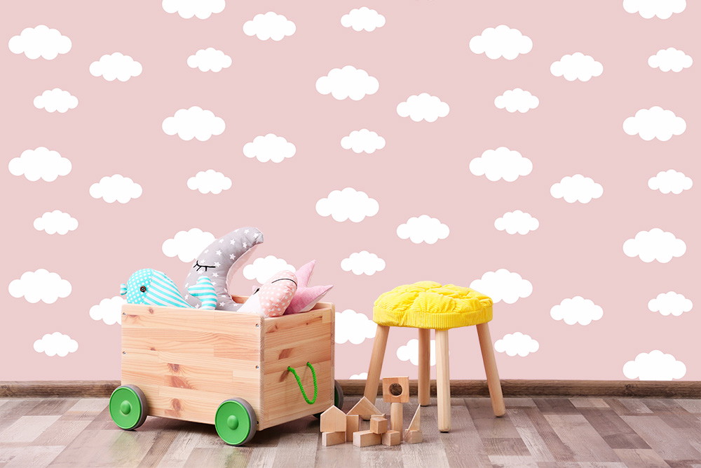 Wall mural - children's room with pink wallpaper and white clouds, a wooden box with colourful toys and a yellow stool