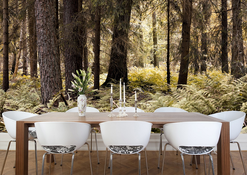 Wall mural - forest motifs in the dining room: wooden table and white chairs in front of a forest full of tall trees and green ferns.