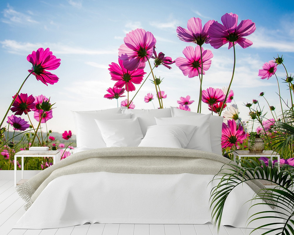 Fototapete - Zimmer mit einem großen Bett vor einer Tapete mit rosa blühenden Blumen und blauem Himmel