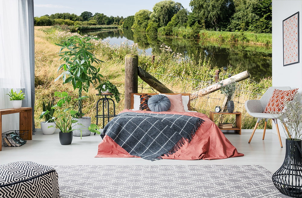 Papier peint photo - chambre à coucher avec vue sur un paysage de rivière à travers une fenêtre, décoration rustique avec des plantes et des draps confortables