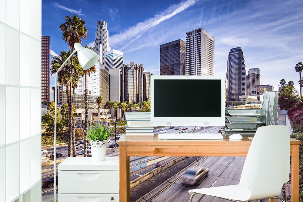 Wall mural - Desk in office with skyline of a big city in the background, modern interior with computer and plants