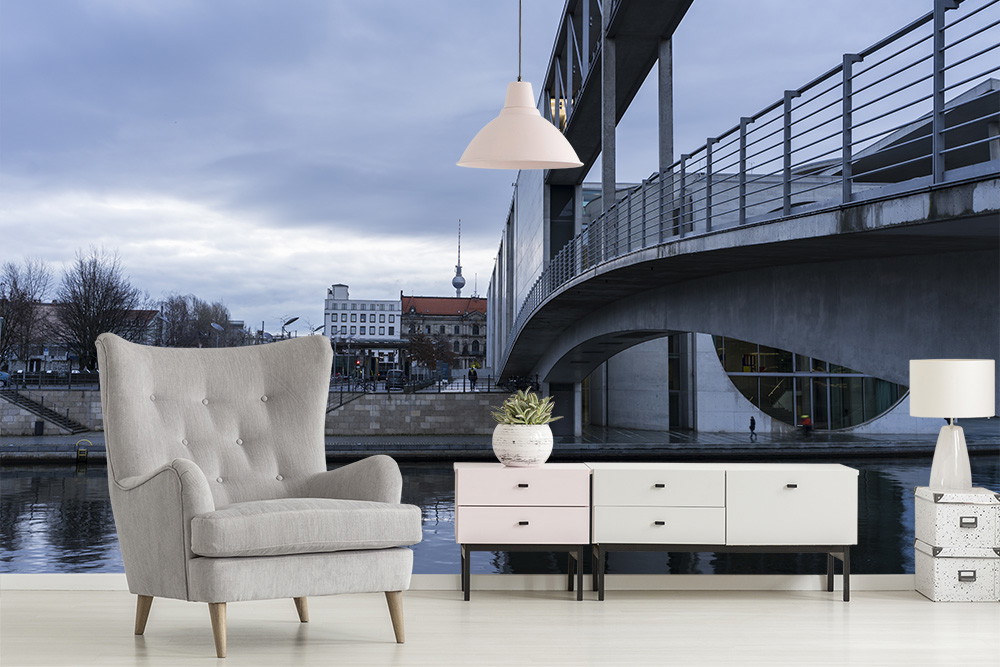 Fototapete - Wohnzimmer mit grauem Sessel und Kommode vor Stadt- und Brückenhintergrund