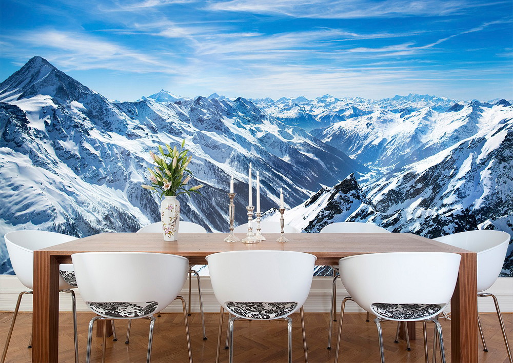 Fototapete - Panorama einer schneebedeckten Berglandschaft hinter einem Esszimmer mit Holz-Esstisch, weißen Stühlen und Blumenvase