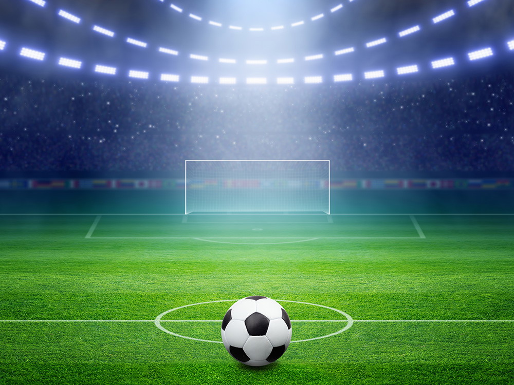 Wall mural - Football in a stadium on a green pitch in front of a goal under floodlights