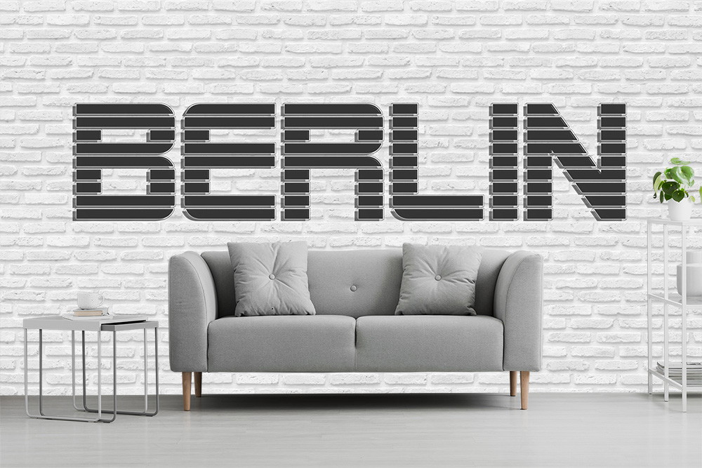 Fototapeta - Szara sofa przed białą ceglaną ścianą z napisem Berlin wypisanym czarnymi literami.