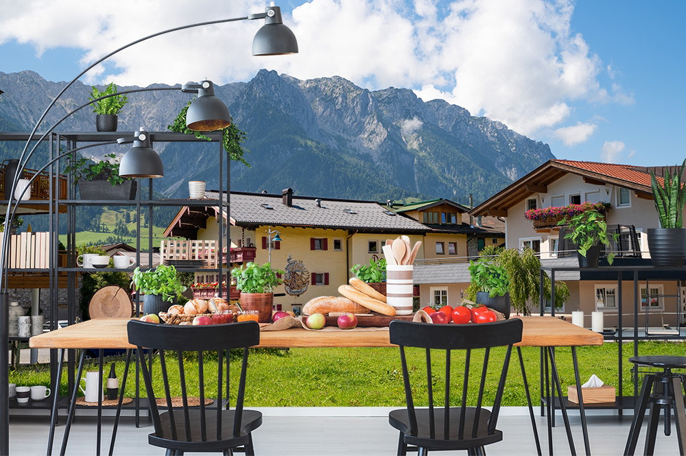 Wall mural - Dining room with wooden table and chairs in front of a picturesque mountain panorama
