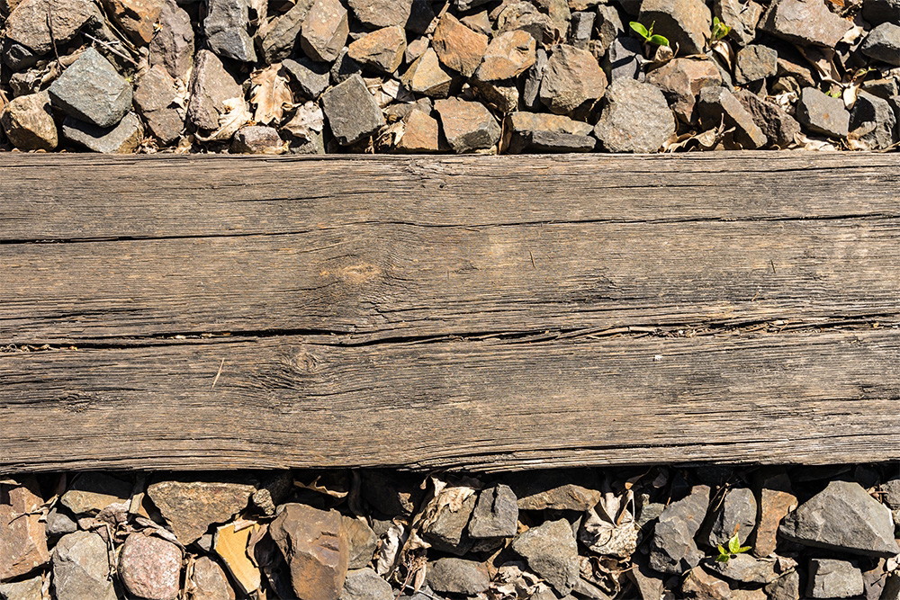 Muurschildering - Close-up van een rustieke houten balk omringd door kleine stenen en kiezels in een natuurlijke omgeving