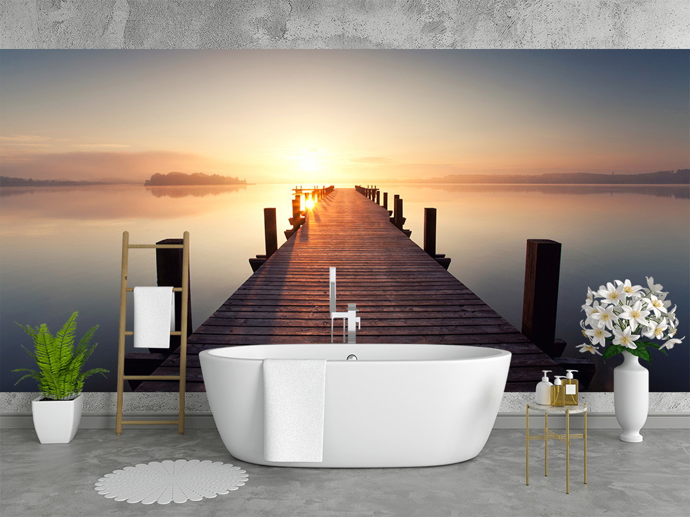 Papier peint photo - paysage avec lever de soleil et passerelle sur un lac tranquille dans une salle de bain élégamment décorée avec baignoire et plantes