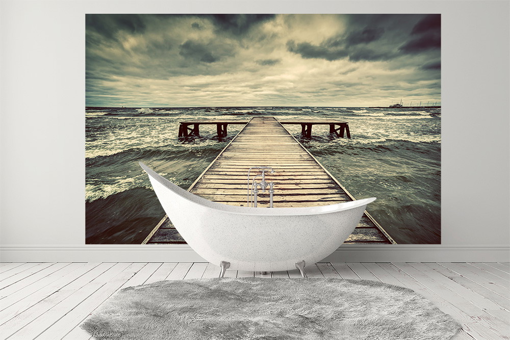 Fototapete - Blick auf einen hölzernen Steg, der in ein stürmisches Meer führt, montiert hinter einer freistehenden Badewanne in einem modernen Badezimmer