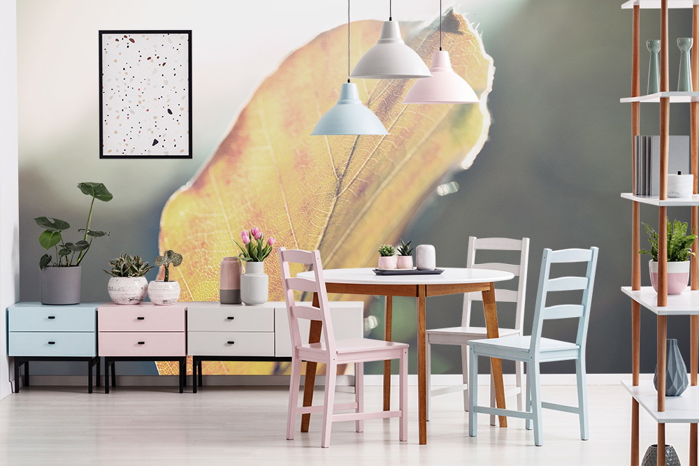 Fotobehang - Stijlvolle eetkamer met een groot, gedetailleerd bladmotief aan de muur, omringd door moderne meubels en planten