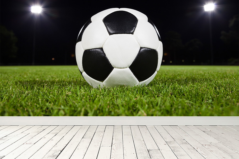 Fototapete - Ein Fußball liegt auf einem grünen Rasen unter Flutlicht auf einem nächtlichen Fußballplatz