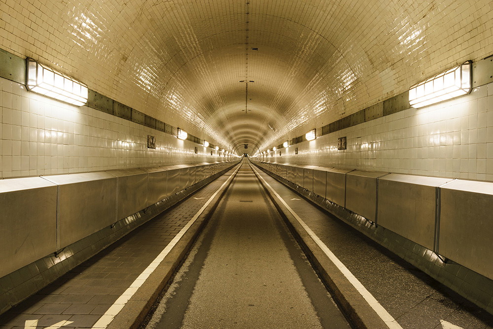 Wall mural - Illuminated tunnel with white tiles and long, symmetrical perspective