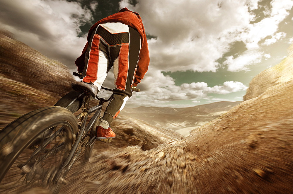 Wall mural - Dynamic image of a mountain biker in red clothing on a dusty, winding path in a mountain landscape with a cloudy sky