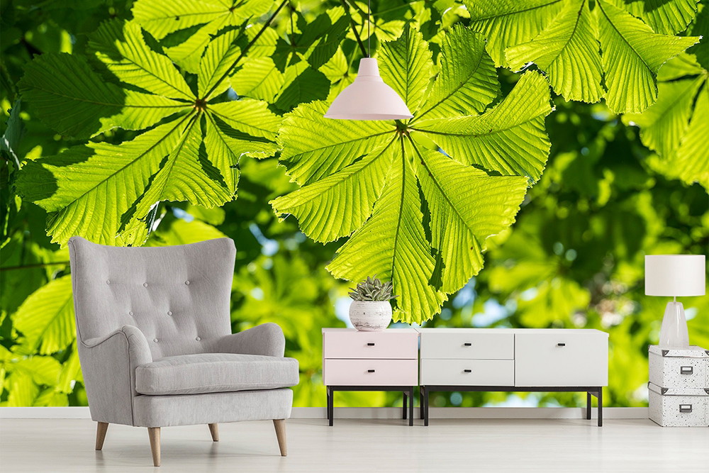 Fototapete - Wohnzimmer mit hellgrauem Sessel, Kommode und großer grüner Blätterwand im Hintergrund