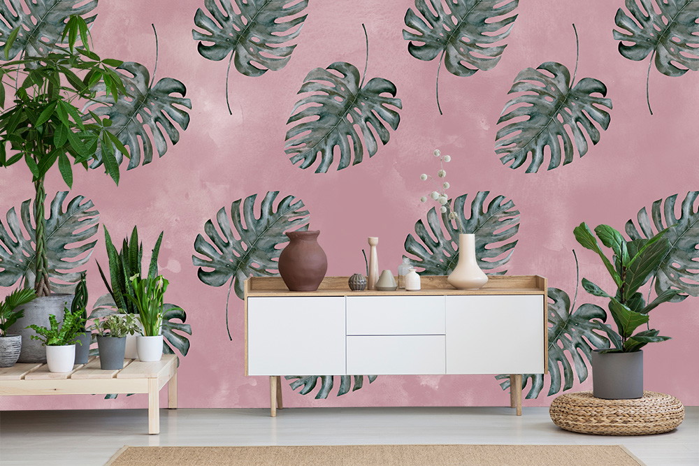 Wall mural - living room with decorative wall mural showing green monstera leaves on a pink background, complemented by modern furniture and houseplants