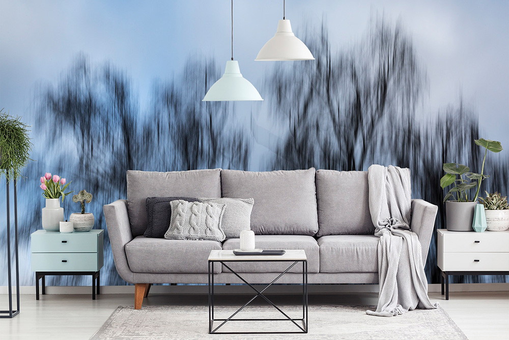 Papier peint photo - Salon élégant avec un canapé gris confortable, des coussins décoratifs et des plantes, en arrière-plan une décoration murale abstraite avec des structures d'arbres floues