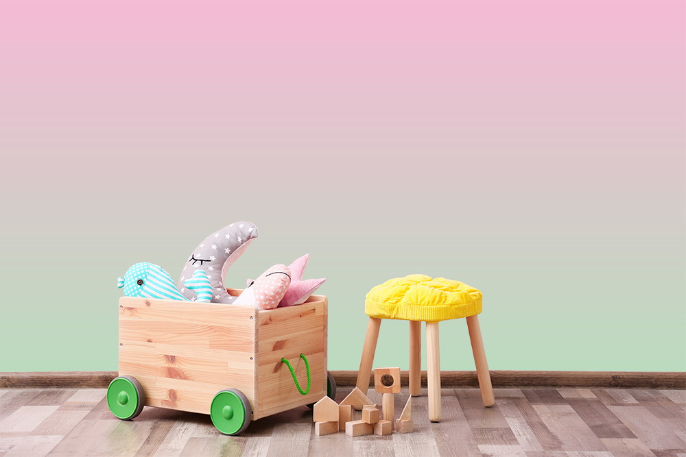 Fototapete - Spielzeugkiste mit Kuscheltieren und gelbem Hocker vor einem rosa und grünen Farbverlauf im Kinderzimmer
