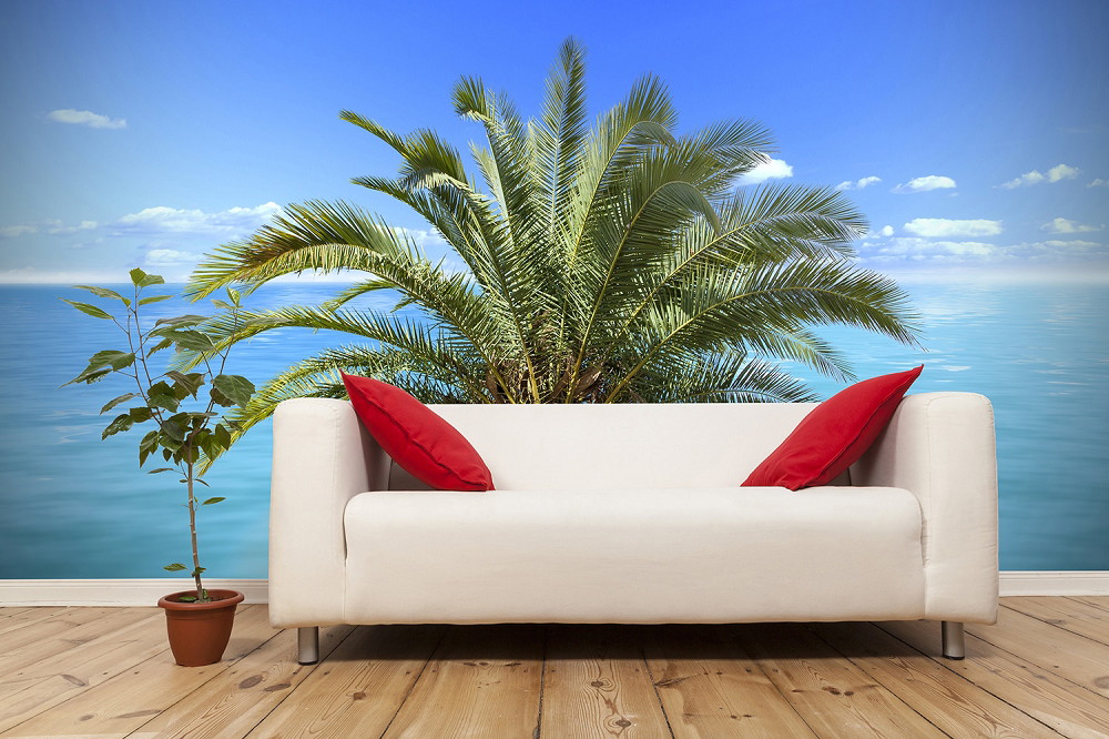 Wall mural - White sofa with red cushions, in front of a wall with palm trees and ocean background, next to a potted plant on a wooden floor