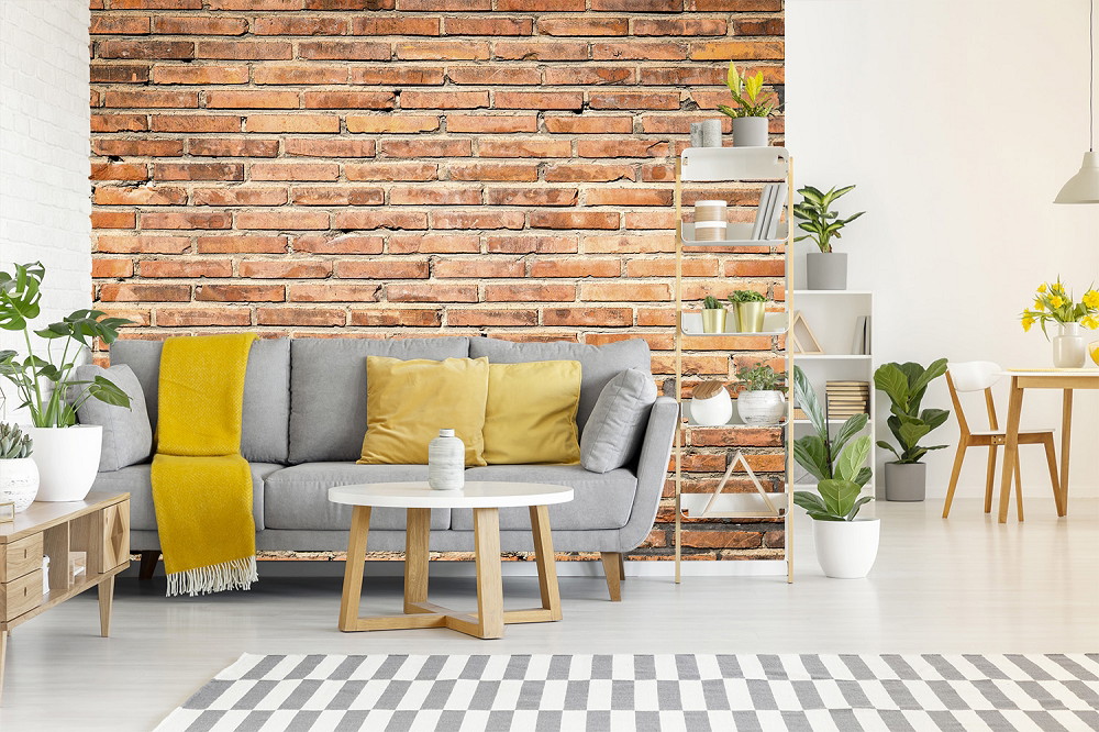 Fotobehang - Woonkamer met grijze bank, bakstenen muur en planten in Scandinavische stijl