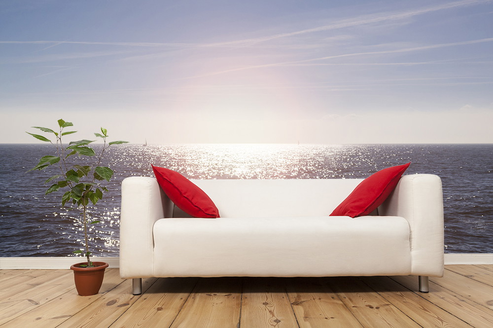 Fototapeta - Biała sofa z czerwonymi poduszkami przed dużą tapetą z widokiem na morze i rośliną doniczkową obok niej