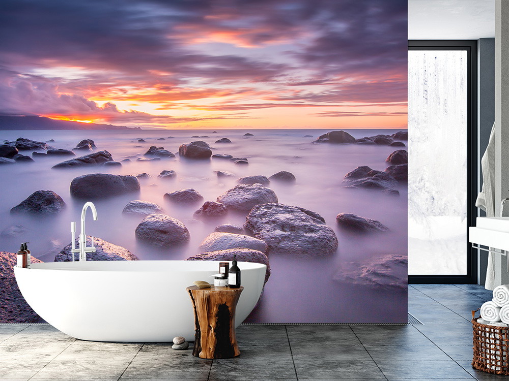 Fototapete - Badezimmer mit weißer Badewanne und Tapete eines Sonnenuntergangs über Felsen am Meer
