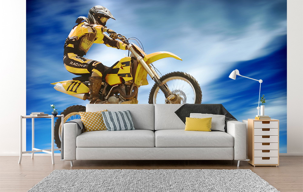 Fototapete - Wohnzimmer mit Couch und aufregendem Motocross-Fahrer auf gelbem Motorrad vor dynamischem blauen Hintergrund