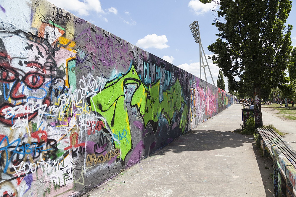 Wall mural - Colourful graffiti on a long wall with park and light pole in the background