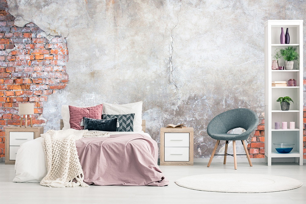 Papier peint photo - chambre à coucher avec un mur de briques rustique, un lit avec des coussins confortables, un fauteuil moderne et une étagère avec des décorations