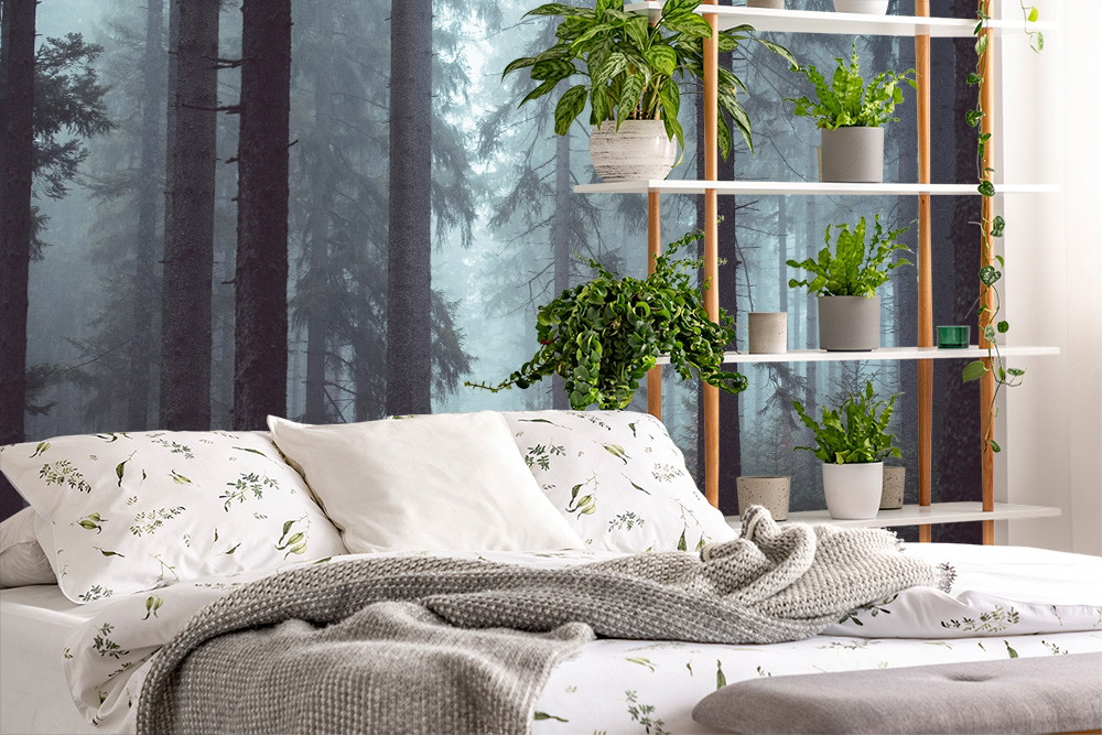 Wall mural - bedroom with forest scenery on the wall, bed with white pillows and blanket and plants on shelves