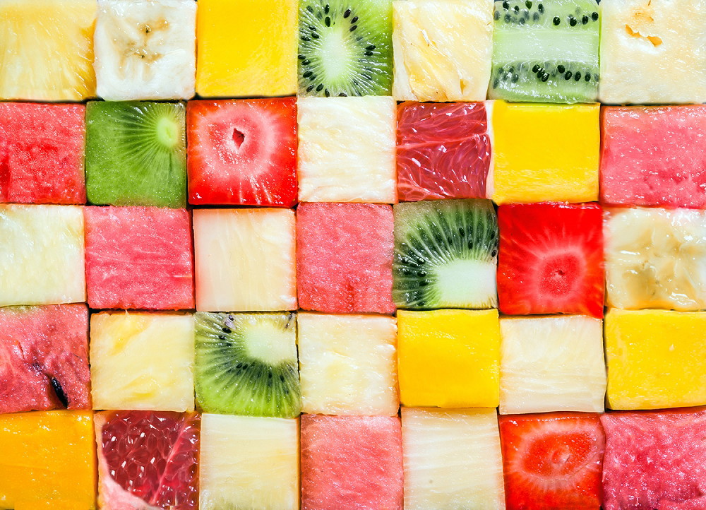 Muurschildering - close-up van fruitblokjes zoals kiwi, aardbei, ananas en watermeloen, gerangschikt in een kleurrijk dambordpatroon