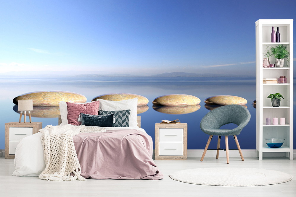 Fototapete - Stilvolles Schlafzimmer mit blauer See-Fototapete und schwebenden Steinen, Bett mit rosa Decke und Regale