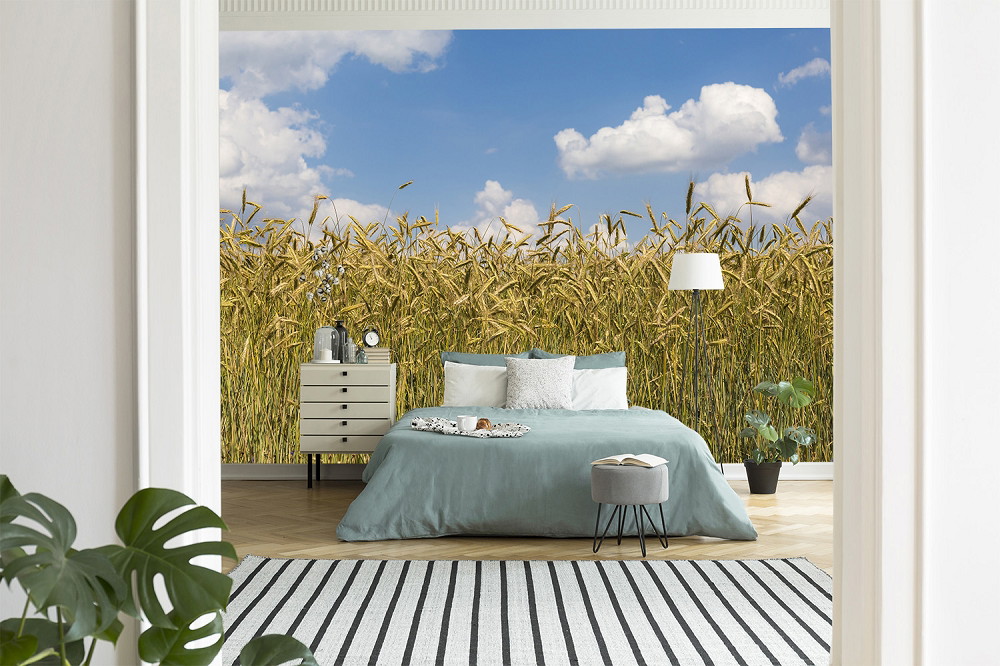 Fotobehang - Slaapkamer met bed, planten en behang met een korenveld onder een blauwe lucht