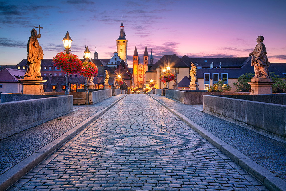 Fototapete - Abendstimmung auf der alten Mainbrücke in Würzburg mit Statuen und Stadtansicht im Hintergrund