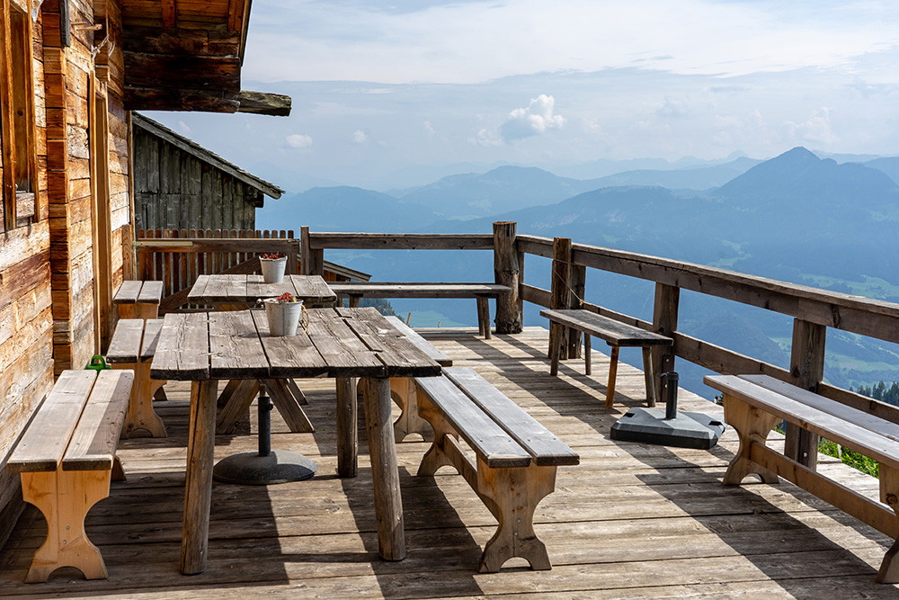 Wall mural - Wooden terrace of a mountain hut with table and benches, surrounded by mountain panorama