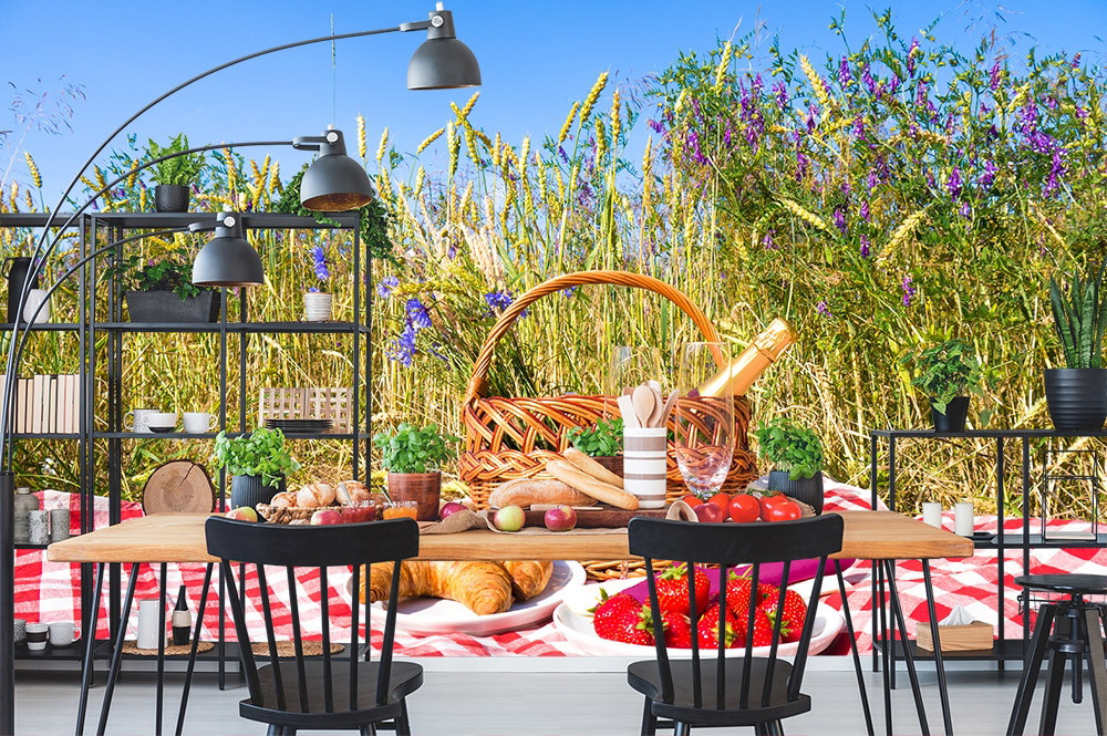 Fototapete - Einladendes Picknick im Freien mit Korb, Brot, Obst und Wein vor blühendem Kornfeld