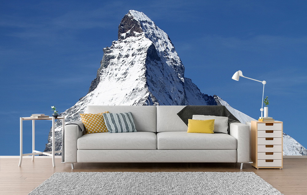Photo wallpaper - Bright living room with comfortable couch, side table, lamp and a photo wallpaper of the snow-covered Matterhorn.