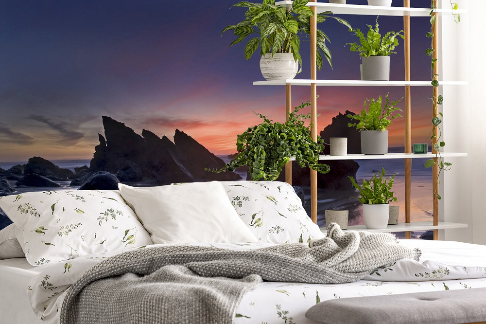 Fototapete - Atemberaubender Sonnenuntergang am Strand, Dekoration mit luxuriösem Bett und Pflanzenregal im Vordergrund