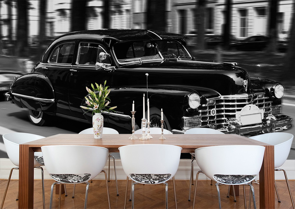 Muurschildering - Zwarte oldtimer rijdt door een straat, op de voorgrond een moderne eethoek met tafel en stoelen