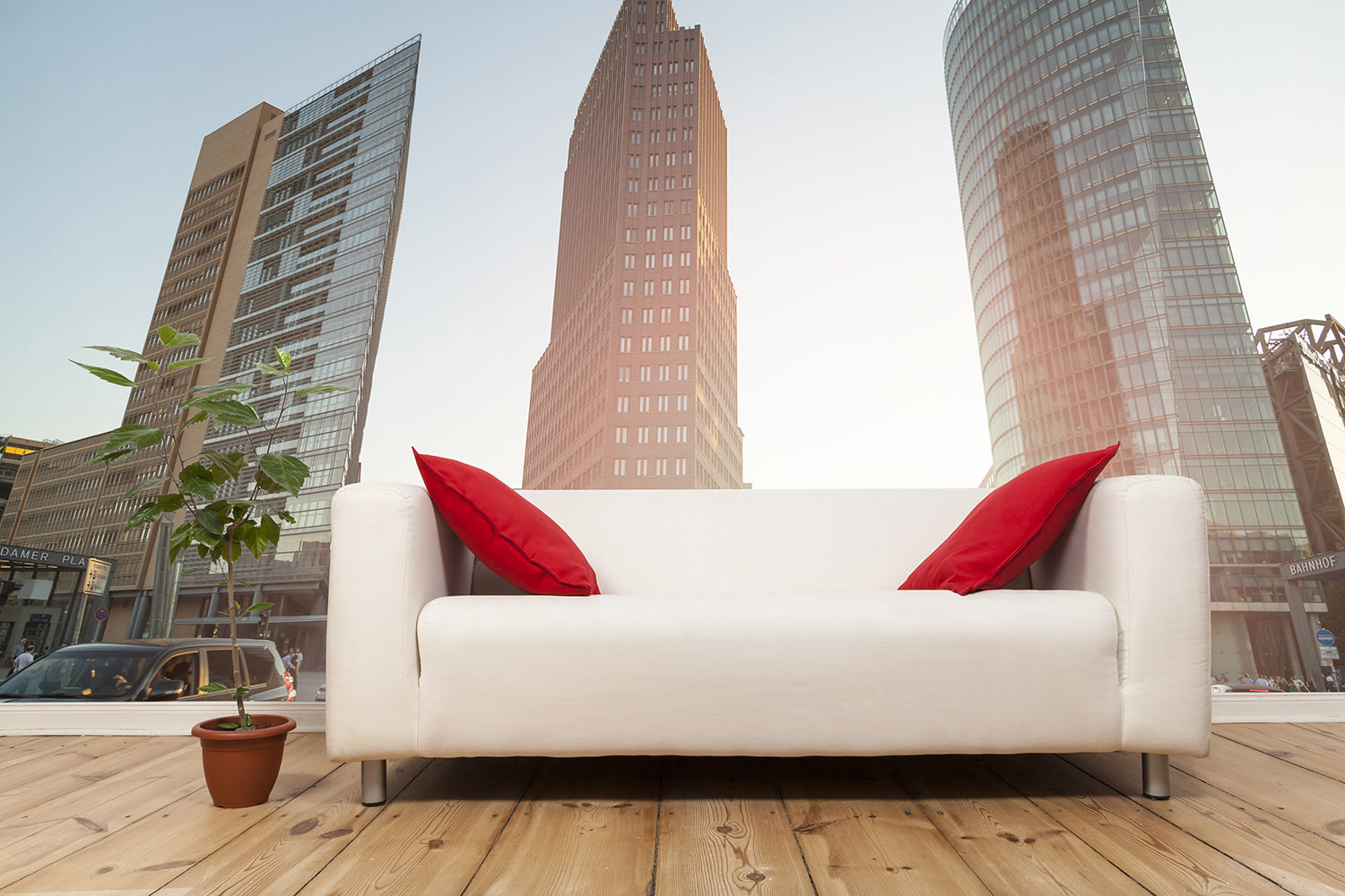 Fototapete - Wohnzimmer mit weißem Sofa, roten Kissen und Blick auf moderne Hochhäuser