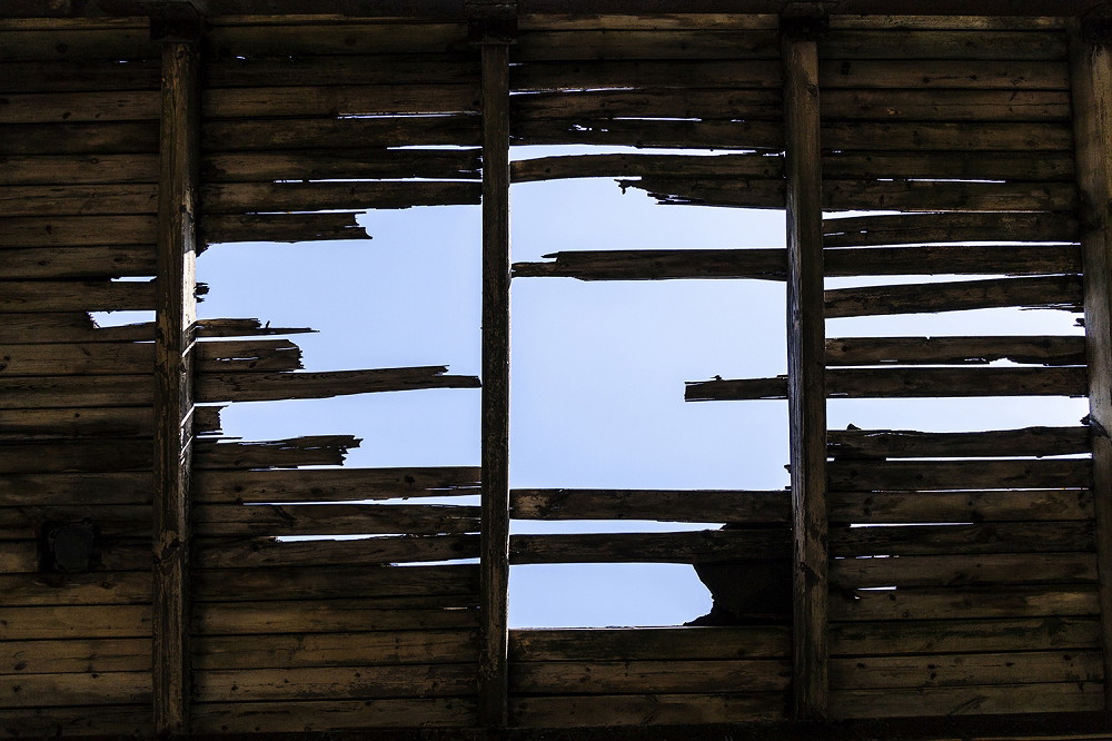 Muurschildering - Verweerd hout van een dak met een gat dat de blauwe lucht laat zien