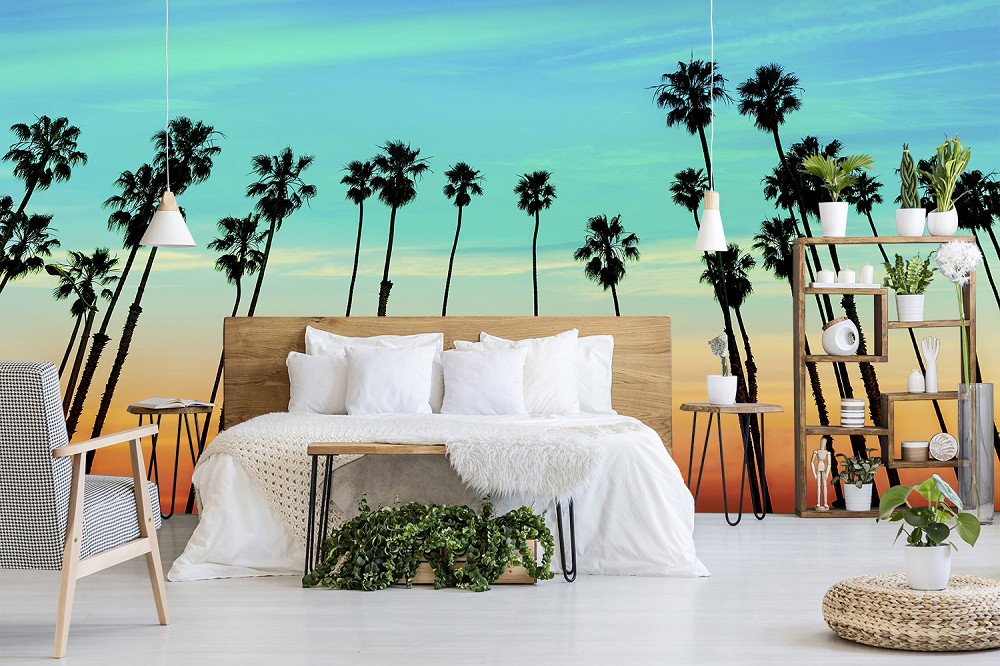 Fotobehang - Moderne slaapkamer met silhouetten van palmbomen tegen een kleurrijke zonsondergang als wanddecoratie