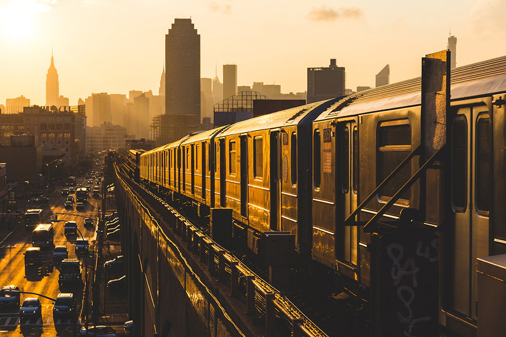 Muurschildering - Een ondergrondse trein rijdt door de stedelijke omgeving voor een skyline bij zonsondergang
