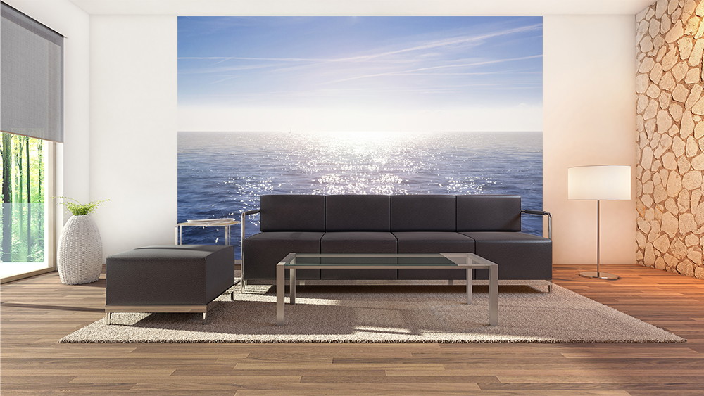 Fototapete - Helles Wohnzimmer mit gemütlichem Sofa vor einer großen Wand mit Meeresmotiv und glänzender Wasseroberfläche